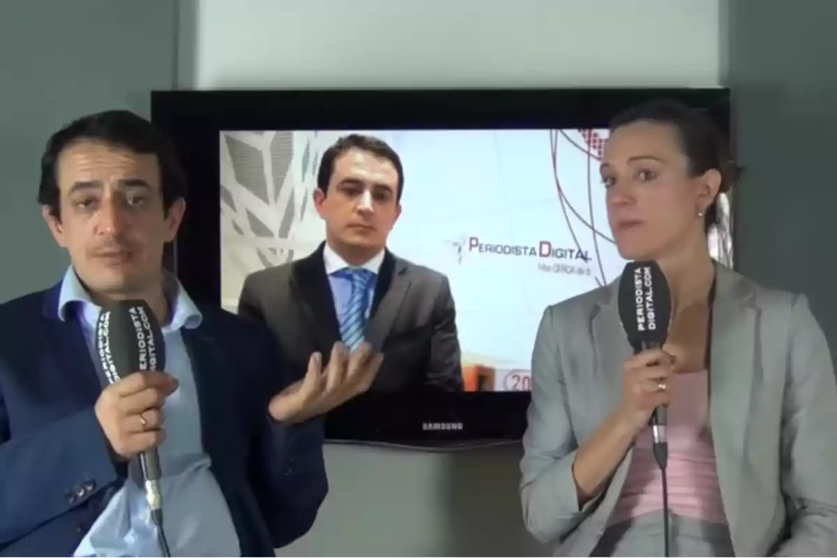 Dos personas con micrófonos de Periodista Digital están sentadas frente a una pantalla que muestra a un hombre en traje y corbata Dos personas con micrófonos de Periodista Digital están sentadas frente a una pantalla que muestra a un hombre en traje y corbata