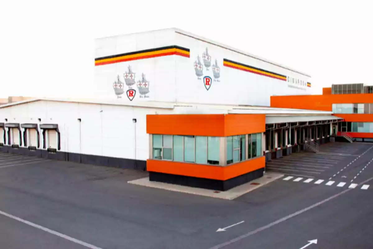 Edificio industrial moderno con detalles naranjas y zona de carga para camiones Edificio industrial moderno con detalles naranjas y zona de carga para camiones