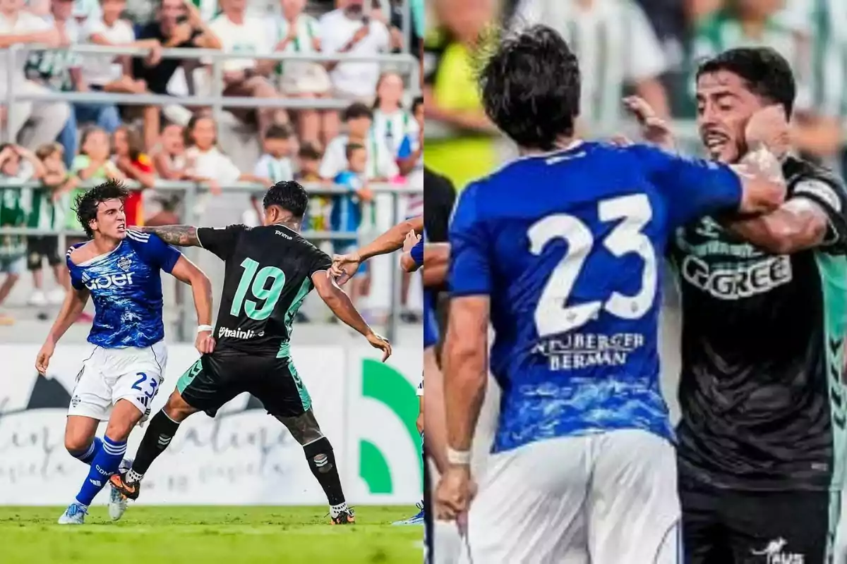 Dos futbolistas de diferentes equipos se enfrentan de manera agresiva durante un partido, uno con uniforme azul y el otro con uniforme negro, mientras el público observa desde las gradas.
