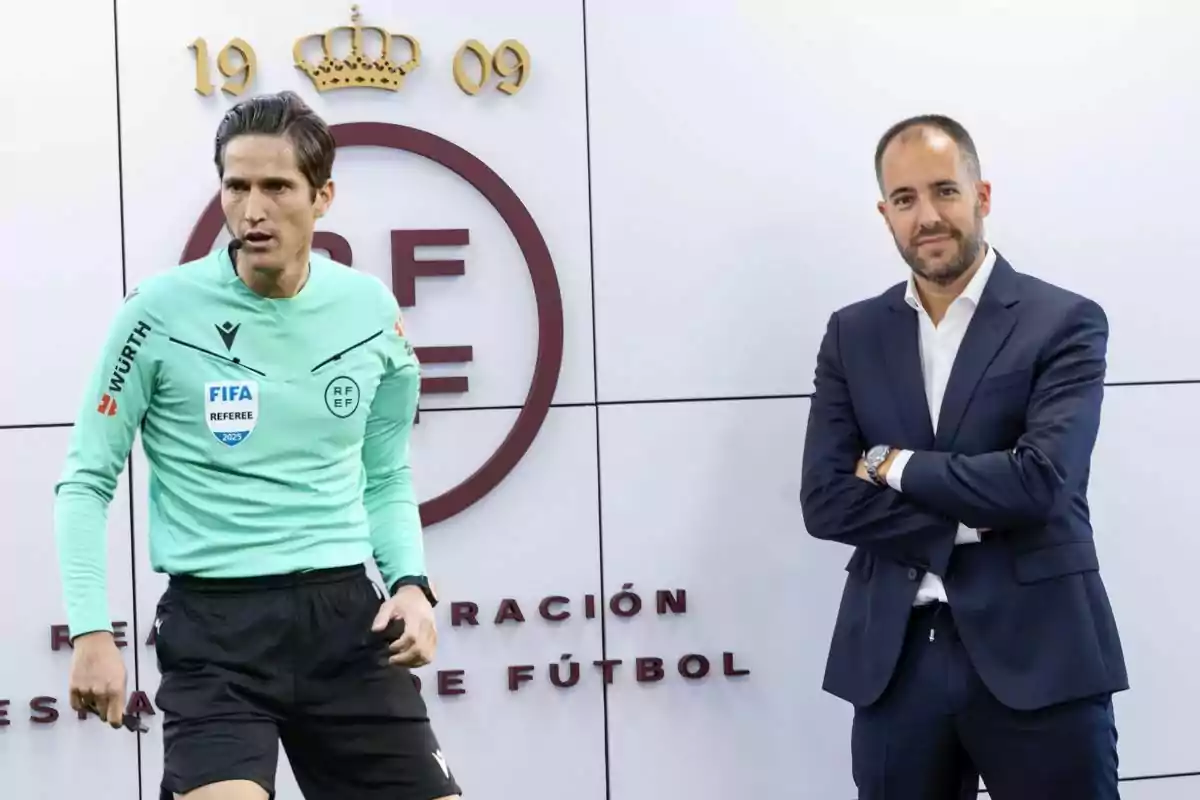 Un árbitro de fútbol con uniforme verde claro y un hombre de traje posan frente a un fondo con el logo de la Real Federación Española de Fútbol.
