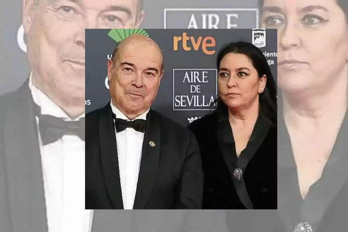 Pareja vestida de gala posando en una alfombra roja frente a un fondo con logotipos de patrocinadores.