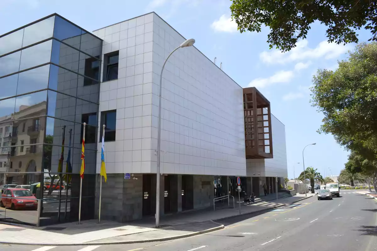 Edificio moderno de fachada blanca y ventanales de cristal ubicado en una calle con árboles y banderas en la entrada