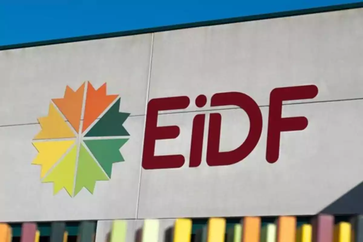 Logo de la empresa EiDF en la fachada de un edificio con un diseño geométrico en tonos verdes y naranjas junto a las letras rojas EiDF Logo de la empresa EiDF en la fachada de un edificio con un diseño geométrico en tonos verdes y naranjas junto a las letras rojas EiDF