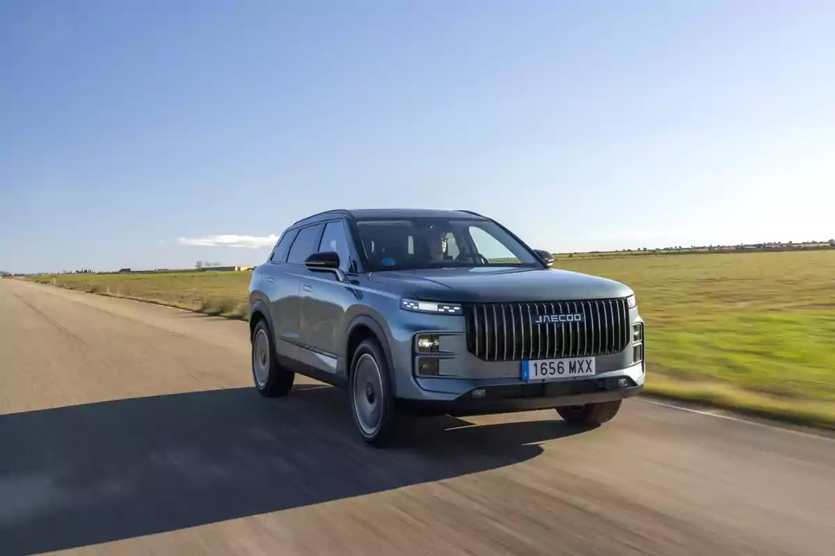 SUV gris circulando por una carretera despejada en medio del campo bajo un cielo azul SUV gris circulando por una carretera despejada en medio del campo bajo un cielo azul
