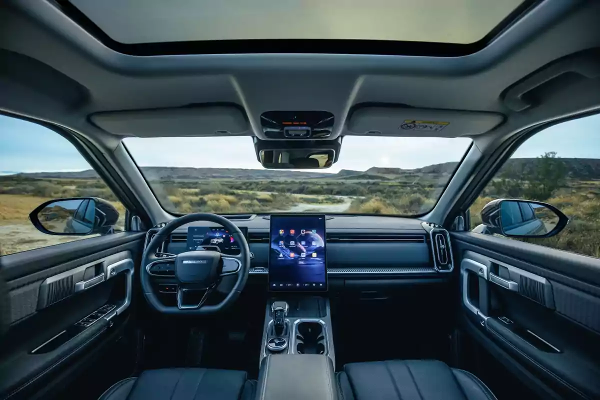 Interior moderno de un automóvil con techo panorámico, pantalla táctil central grande y vista hacia un paisaje desértico a través del parabrisas Interior moderno de un automóvil con techo panorámico, pantalla táctil central grande y vista hacia un paisaje desértico a través del parabrisas