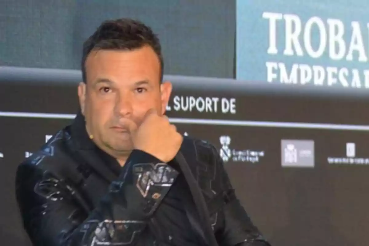 Hombre de cabello corto y oscuro con chaqueta negra sentado en un evento empresarial mirando hacia la cámara con expresión seria
