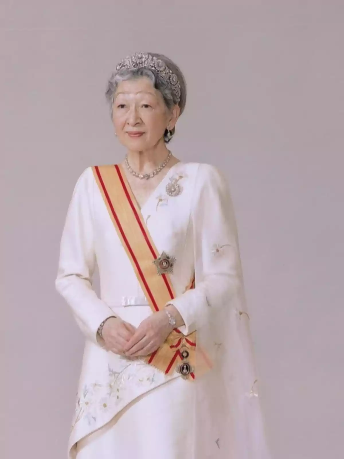 Mujer mayor con vestido blanco elegante, banda amarilla con rojo y tiara plateada, posando frente a un fondo neutro Mujer mayor con vestido blanco elegante, banda amarilla con rojo y tiara plateada, posando frente a un fondo neutro