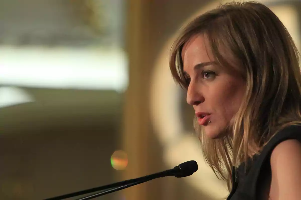 Mujer rubia hablando frente a un micrófono en un ambiente interior iluminado Mujer rubia hablando frente a un micrófono en un ambiente interior iluminado
