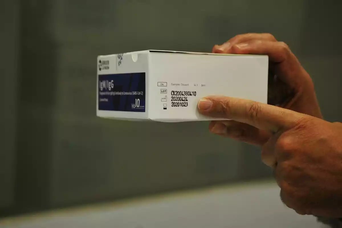 Persona sosteniendo una caja de pruebas rápidas de anticuerpos IgM IgG para SARS-CoV-2 con información de lote visible en el costado. Persona sosteniendo una caja de pruebas rápidas de anticuerpos IgM IgG para SARS-CoV-2 con información de lote visible en el costado.