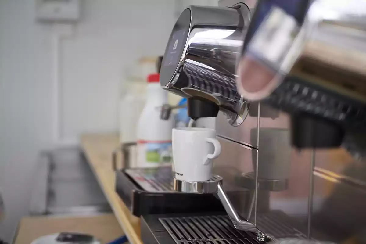 Una taza blanca colocada en una máquina de café espresso en una barra de cocina Una taza blanca colocada en una máquina de café espresso en una barra de cocina