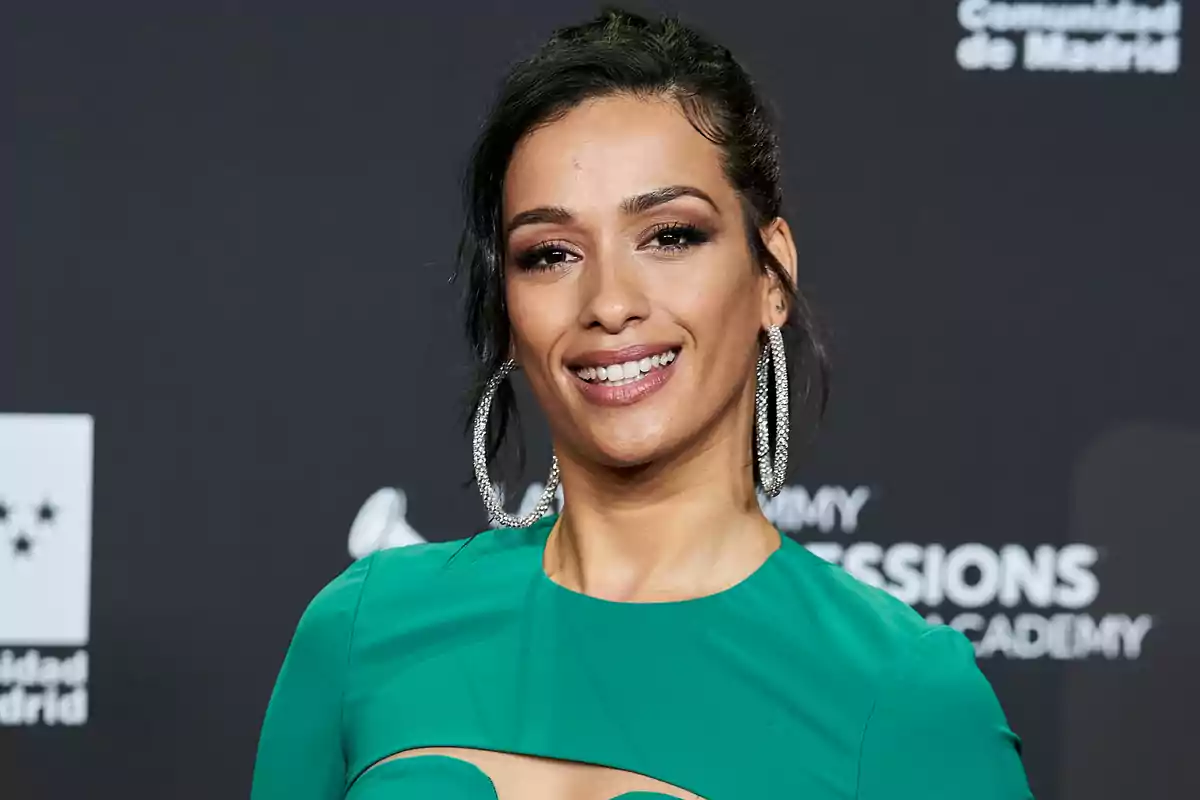 Mujer sonriendo con vestido verde y pendientes grandes en un evento con fondo negro Mujer sonriendo con vestido verde y pendientes grandes en un evento con fondo negro