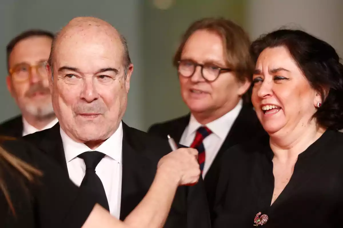 Grupo de personas elegantemente vestidas sonríen y conversan en un evento social