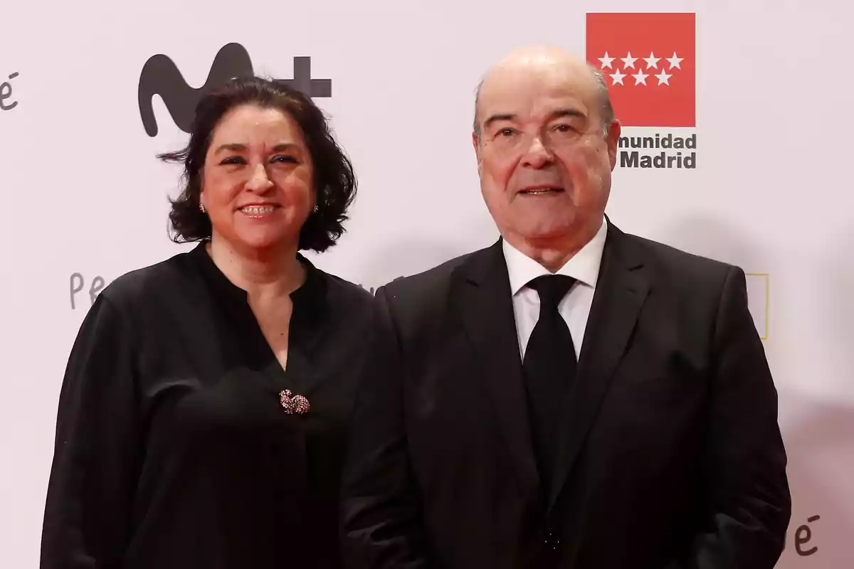 Una mujer y un hombre posan sonrientes en una alfombra roja vestidos de negro con fondo de logotipos y el texto Comunidad de Madrid.