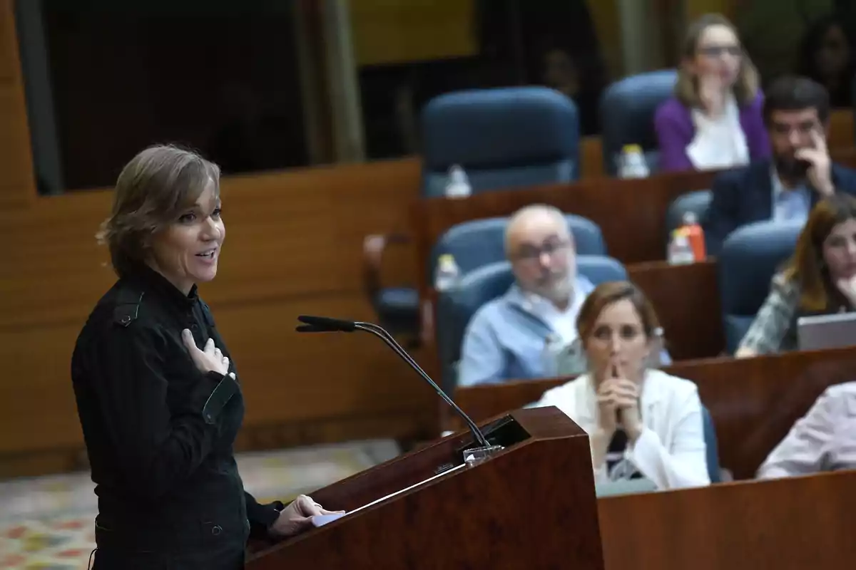 Mujer hablando en un podio frente a una audiencia atenta en una sala de conferencias Mujer hablando en un podio frente a una audiencia atenta en una sala de conferencias