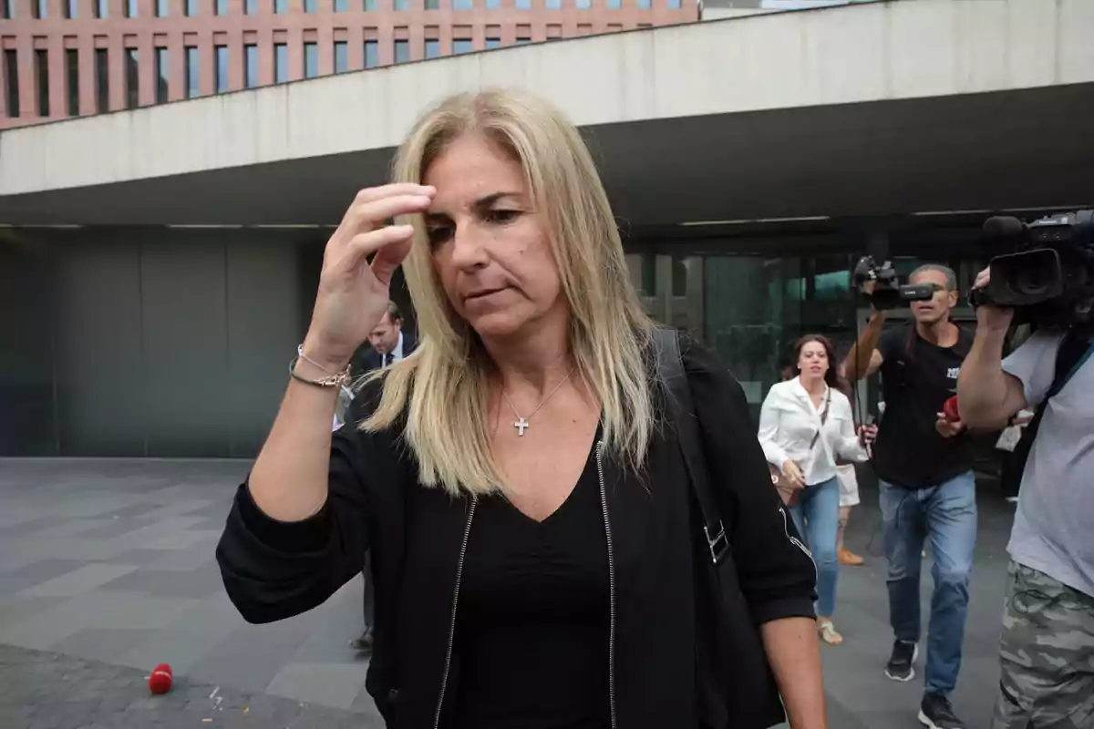 Mujer rubia con expresión seria caminando frente a un edificio mientras es seguida por periodistas y camarógrafos Mujer rubia con expresión seria caminando frente a un edificio mientras es seguida por periodistas y camarógrafos