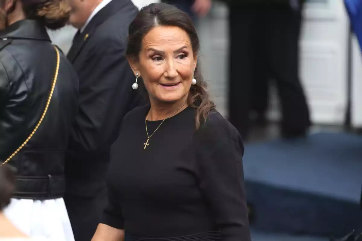 Mujer de cabello castaño recogido vestida de negro con pendientes de perla y collar de cruz en un evento formal al aire libre Mujer de cabello castaño recogido vestida de negro con pendientes de perla y collar de cruz en un evento formal al aire libre