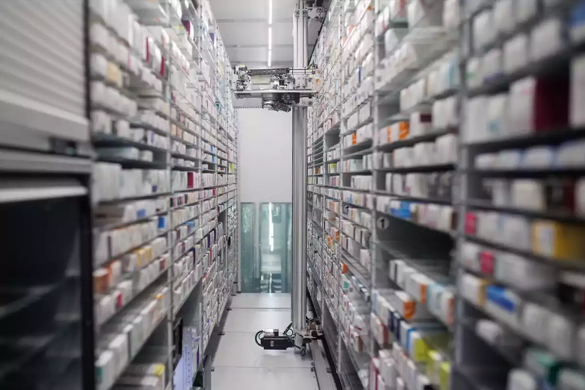 Pasillo de una farmacia automatizada con estantes llenos de cajas de medicamentos y un robot dispensador en el centro