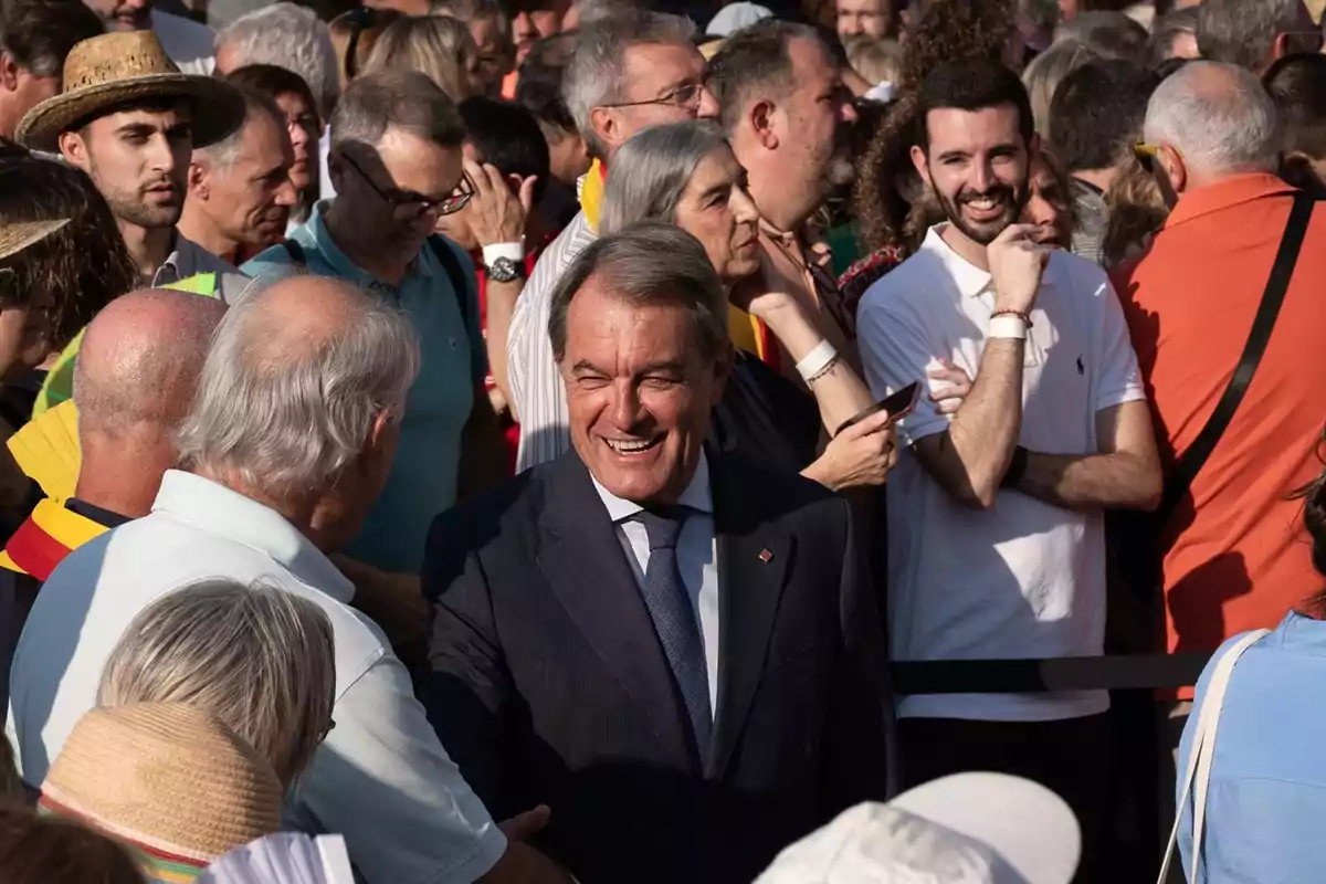 Un hombre de traje sonríe mientras saluda a personas en medio de una multitud durante un evento al aire libre en un día soleado