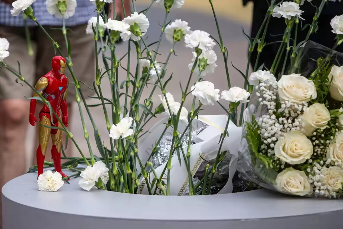 Figura de Iron Man junto a un ramo de flores blancas y rosas en un memorial al aire libre Figura de Iron Man junto a un ramo de flores blancas y rosas en un memorial al aire libre