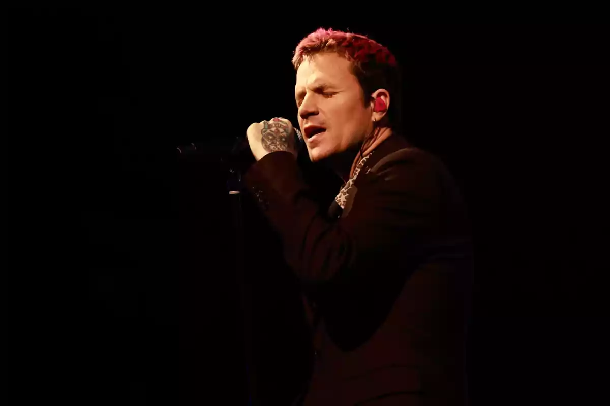 Hombre cantando apasionadamente en el escenario con micrófono en mano y fondo oscuro Hombre cantando apasionadamente en el escenario con micrófono en mano y fondo oscuro