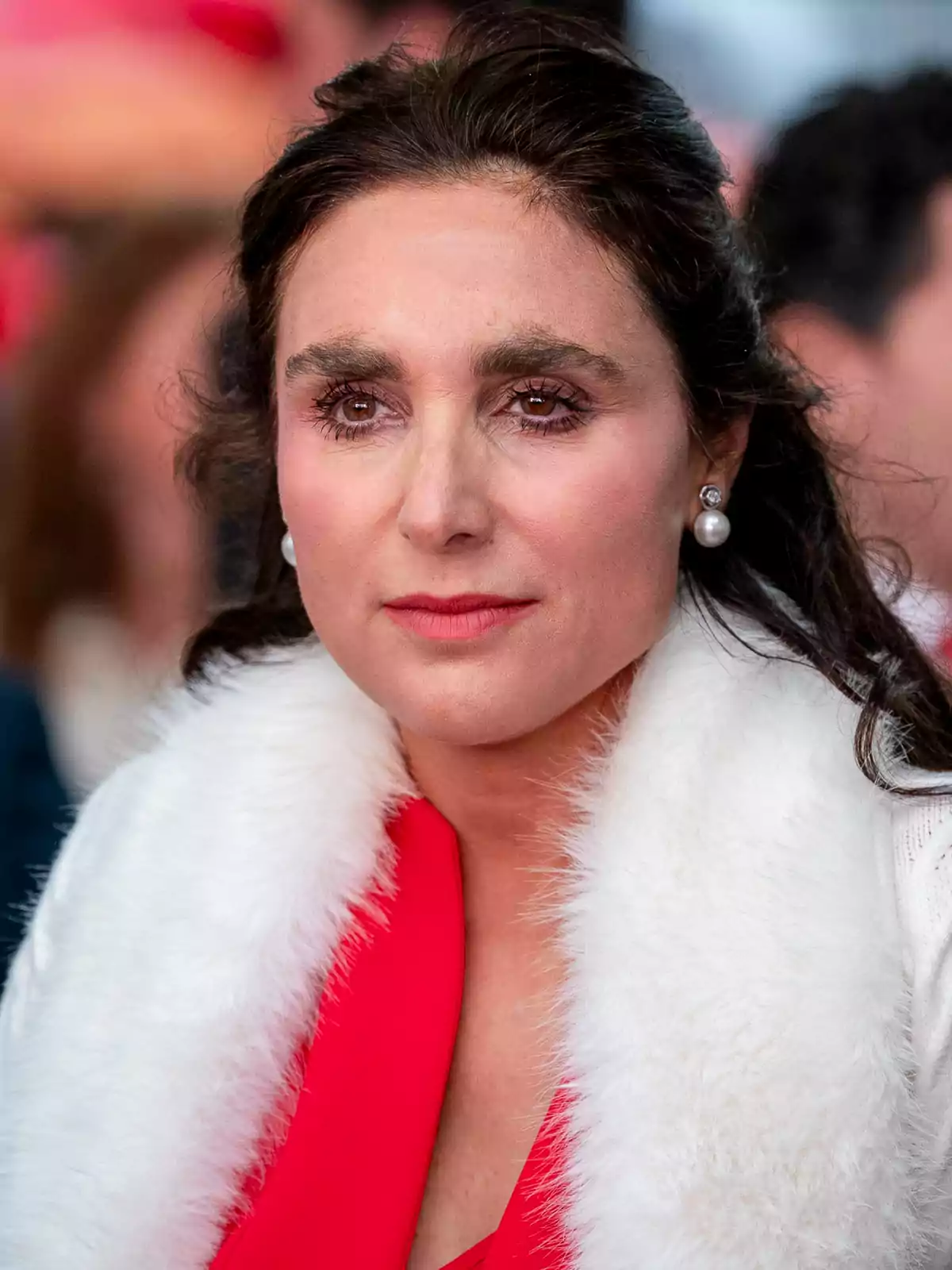 Mujer de cabello oscuro con abrigo blanco de peluche y blusa roja mirando al frente Mujer de cabello oscuro con abrigo blanco de peluche y blusa roja mirando al frente