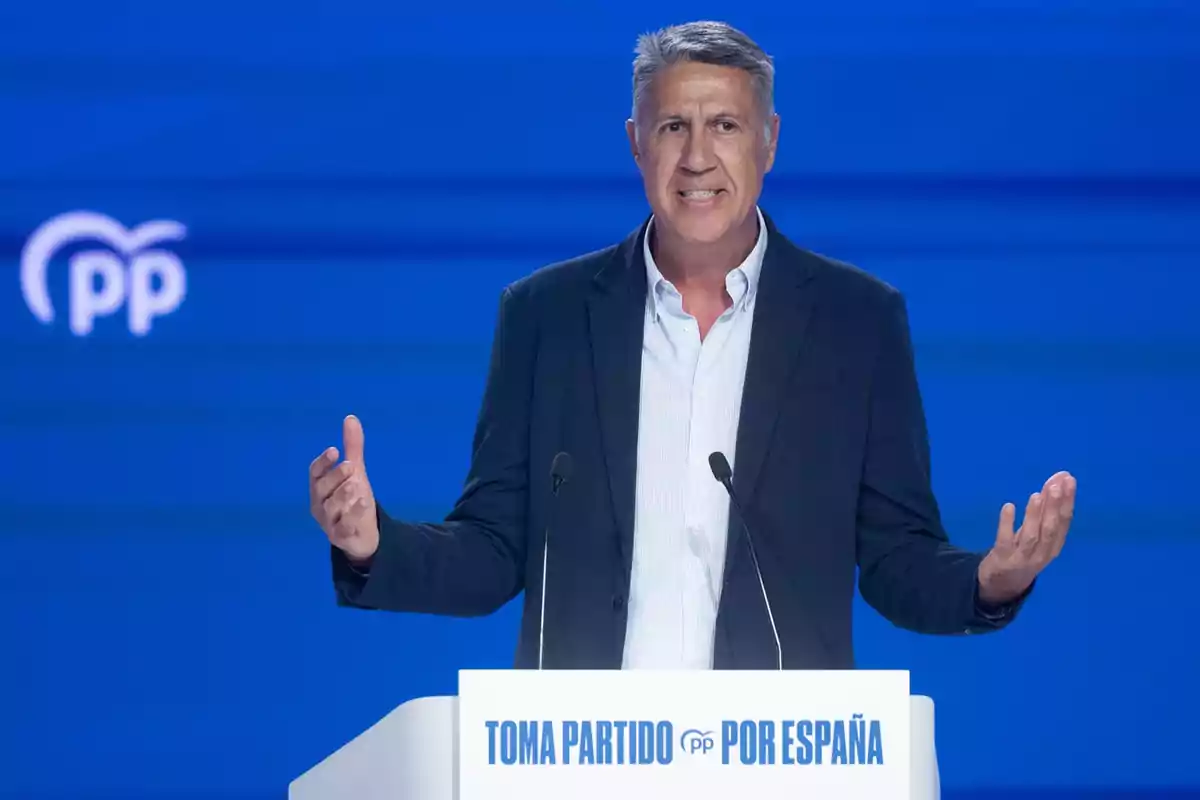 Hombre de cabello canoso hablando en un atril con fondo azul y el logo del Partido Popular de España Hombre de cabello canoso hablando en un atril con fondo azul y el logo del Partido Popular de España