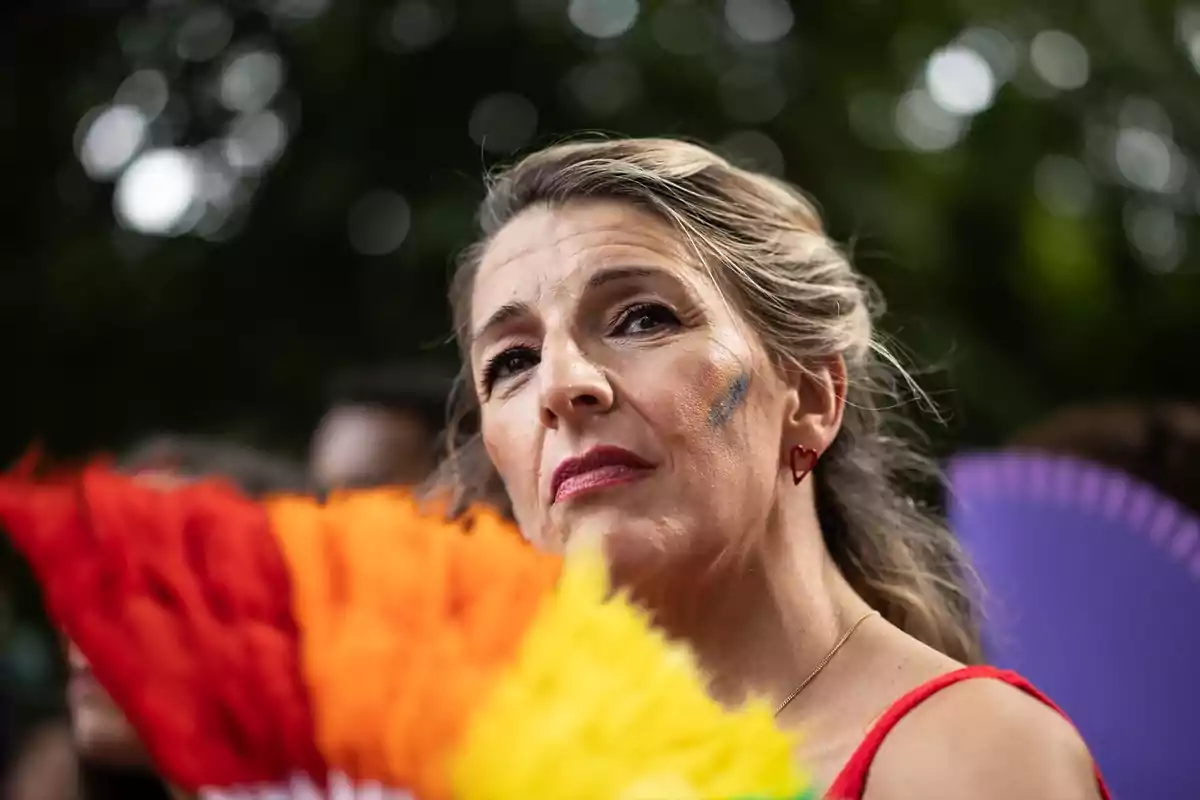 Mujer con abanico de colores y maquillaje de arcoíris en la mejilla durante un evento al aire libre