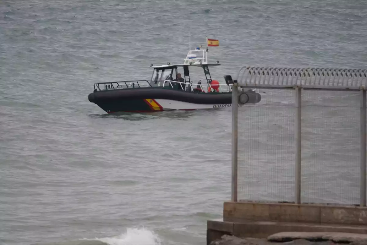 Patrullera de la Guardia Civil navegando cerca de una valla en la costa