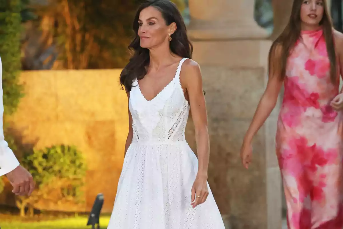 Mujer con vestido blanco de tirantes caminando al aire libre acompañada de otra persona con vestido rosa y fondo de jardín y piedra. Mujer con vestido blanco de tirantes caminando al aire libre acompañada de otra persona con vestido rosa y fondo de jardín y piedra.