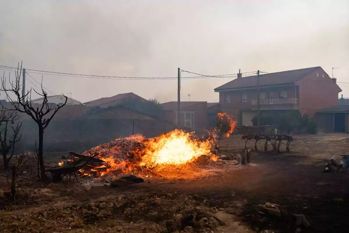 Fuego intenso ardiendo en un terreno cerca de casas de ladrillo en una zona rural