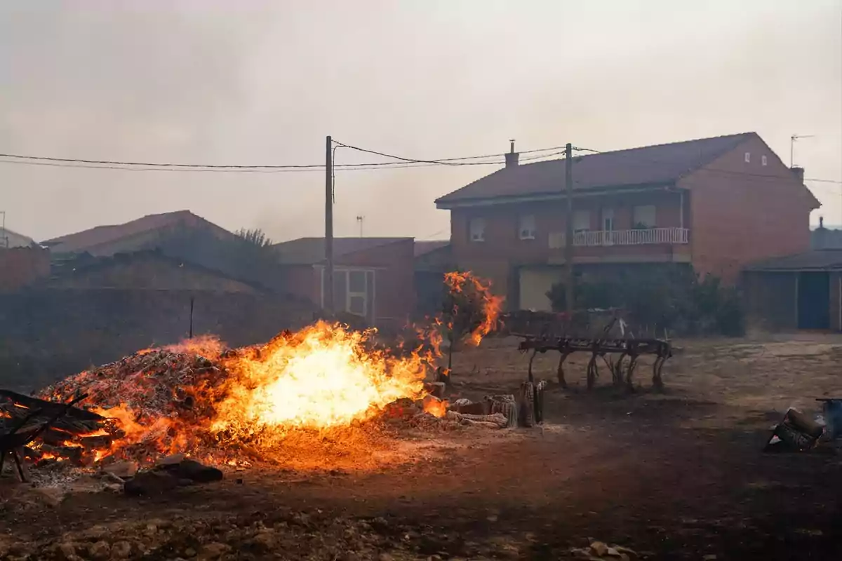 Fuego intenso ardiendo en un terreno cerca de casas de ladrillo en una zona rural Fuego intenso ardiendo en un terreno cerca de casas de ladrillo en una zona rural
