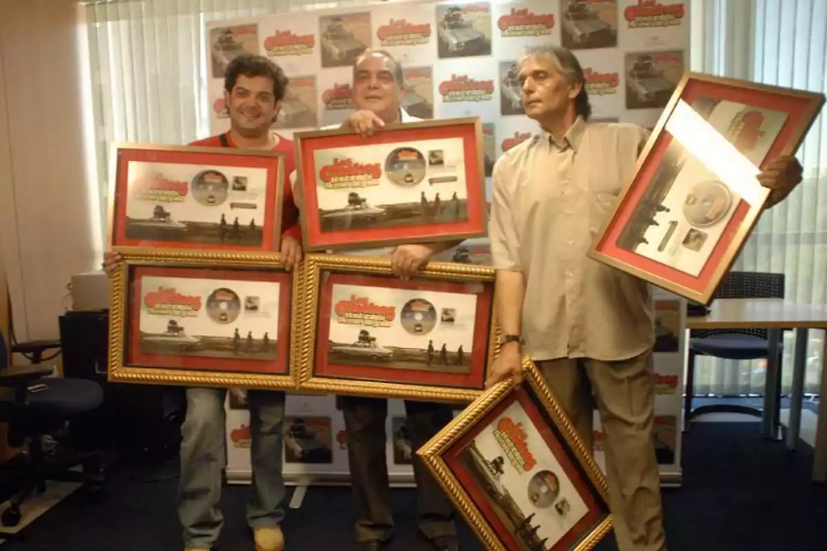 Tres hombres posan sonrientes en una oficina mientras sostienen varios cuadros conmemorativos de la serie Los Güeros del Zodiaco Tres hombres posan sonrientes en una oficina mientras sostienen varios cuadros conmemorativos de la serie Los Güeros del Zodiaco