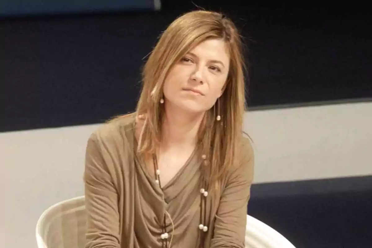 Mujer de cabello rubio lacio sentada en una silla con expresión seria y fondo oscuro Mujer de cabello rubio lacio sentada en una silla con expresión seria y fondo oscuro