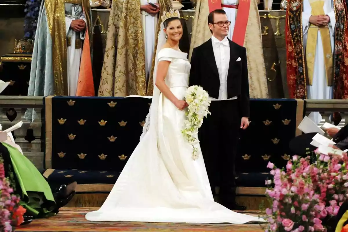 Pareja de novios elegantemente vestidos en una ceremonia de boda rodeados de flores y personas con vestimentas formales en un ambiente decorado de manera lujosa Pareja de novios elegantemente vestidos en una ceremonia de boda rodeados de flores y personas con vestimentas formales en un ambiente decorado de manera lujosa