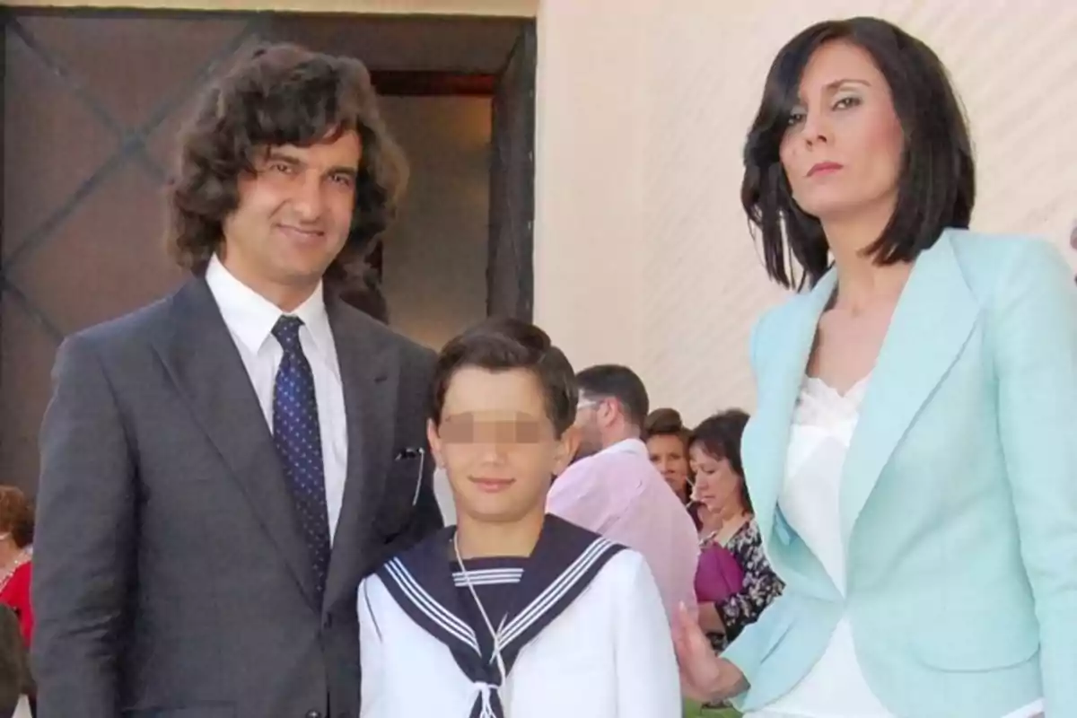 Una familia posa para una foto en un evento formal, el niño lleva un traje de marinero y los adultos visten ropa elegante, al fondo hay más personas. Una familia posa para una foto en un evento formal, el niño lleva un traje de marinero y los adultos visten ropa elegante, al fondo hay más personas.