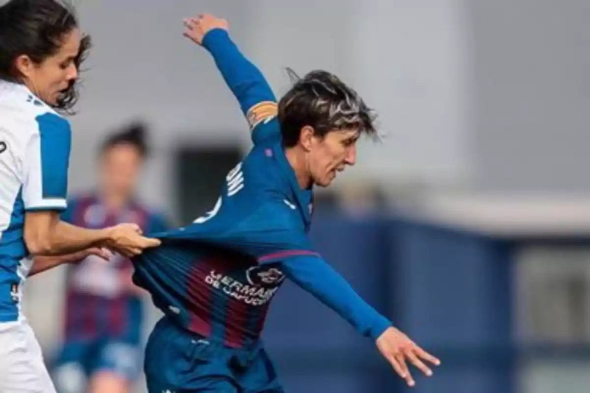 Jugadora de fútbol con uniforme azul es sujetada por la camiseta por una rival durante un partido Jugadora de fútbol con uniforme azul es sujetada por la camiseta por una rival durante un partido