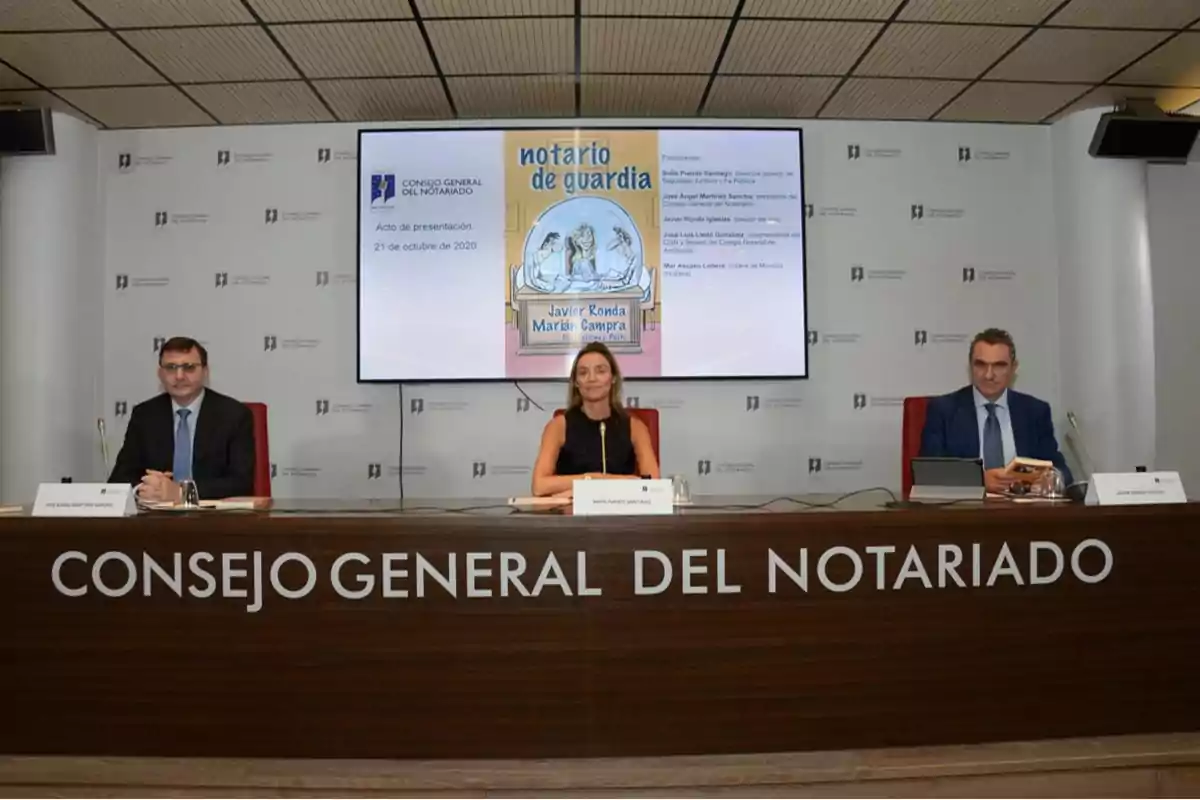Tres personas sentadas en una mesa durante la presentación de un libro titulada Notario de guardia en una sala del Consejo General del Notariado, con una pantalla grande mostrando la portada del libro y detalles del evento.