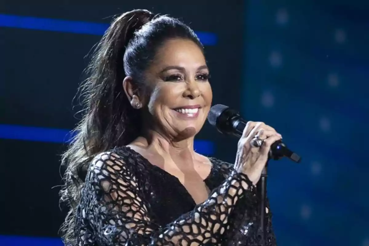 Mujer sonriente con el cabello recogido cantando en un escenario y sosteniendo un micrófono Mujer sonriente con el cabello recogido cantando en un escenario y sosteniendo un micrófono