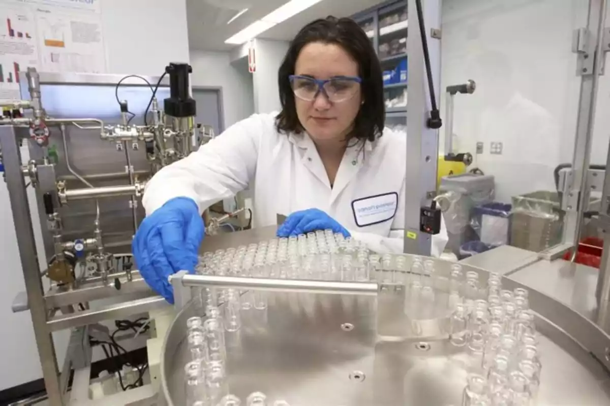 Mujer con bata de laboratorio y guantes azules manipulando frascos de vidrio en un laboratorio científico Mujer con bata de laboratorio y guantes azules manipulando frascos de vidrio en un laboratorio científico