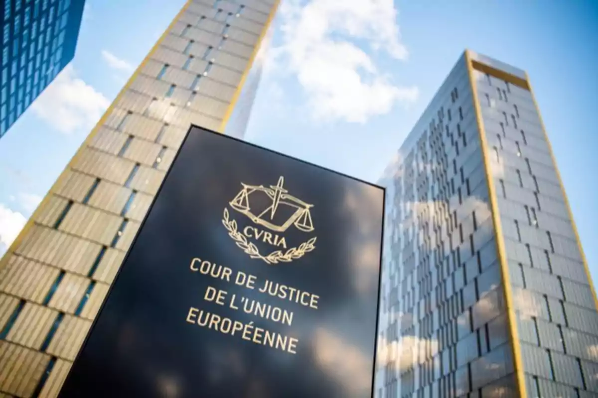 Edificio moderno de la Corte de Justicia de la Unión Europea con un letrero negro en primer plano y dos torres de vidrio al fondo bajo un cielo azul con nubes Edificio moderno de la Corte de Justicia de la Unión Europea con un letrero negro en primer plano y dos torres de vidrio al fondo bajo un cielo azul con nubes