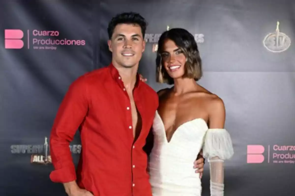 Pareja posando en una alfombra roja, él viste camisa roja y ella lleva un vestido blanco elegante Pareja posando en una alfombra roja, él viste camisa roja y ella lleva un vestido blanco elegante