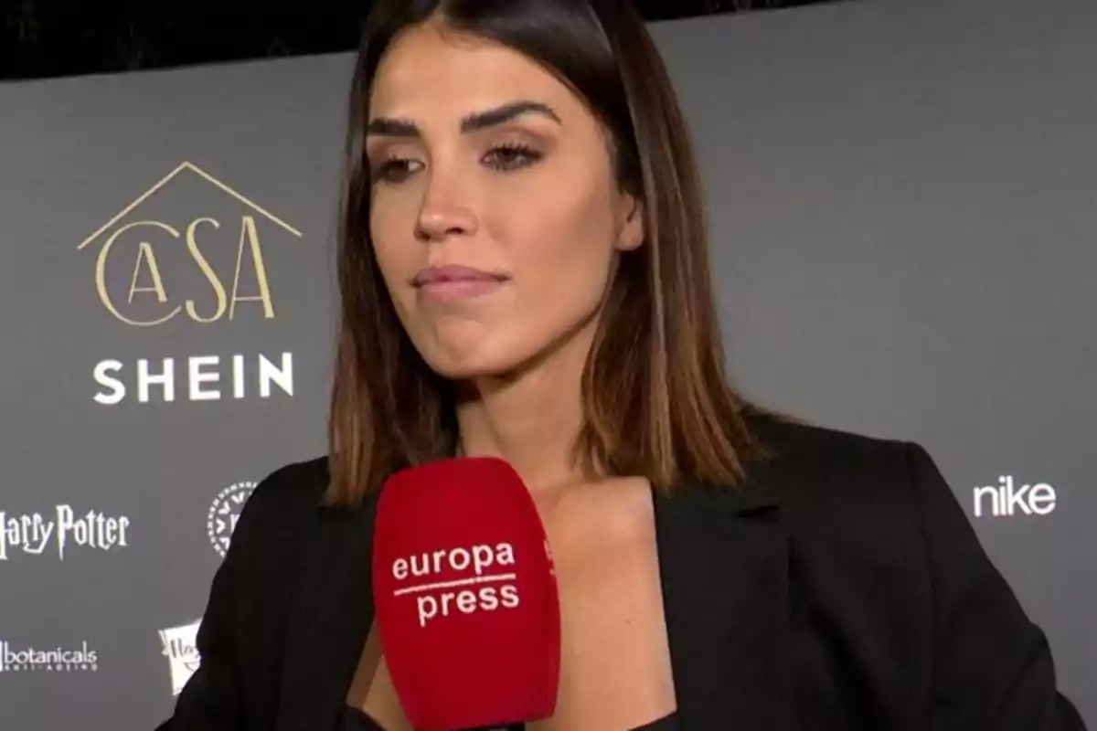 Mujer de cabello castaño y liso con chaqueta negra sosteniendo un micrófono rojo de europa press frente a un fondo con logotipos de marcas. Mujer de cabello castaño y liso con chaqueta negra sosteniendo un micrófono rojo de europa press frente a un fondo con logotipos de marcas.
