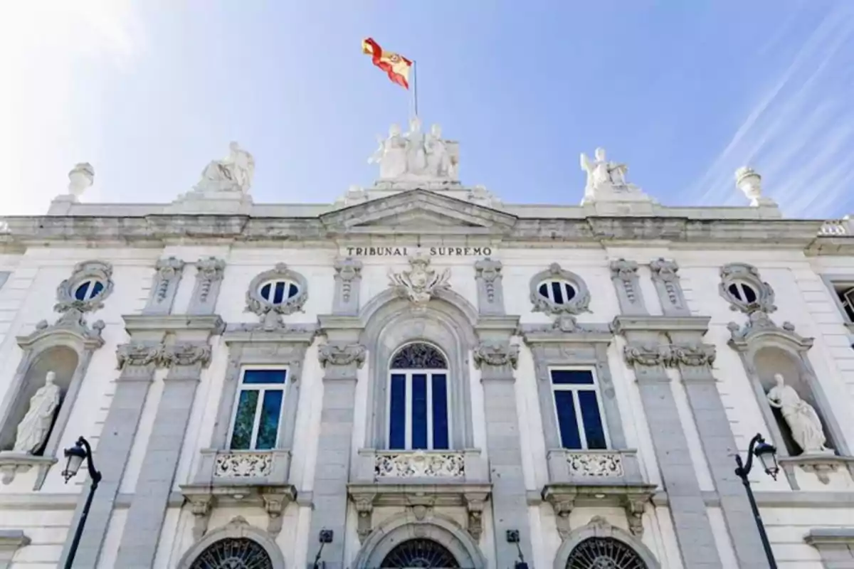 Fachada del Tribunal Supremo de España con la bandera española ondeando en la parte superior del edificio bajo un cielo azul Fachada del Tribunal Supremo de España con la bandera española ondeando en la parte superior del edificio bajo un cielo azul