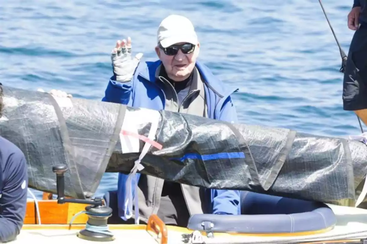 Older man wearing a cap and sunglasses waving while sailing on a sailboat Older man wearing a cap and sunglasses waving while sailing on a sailboat