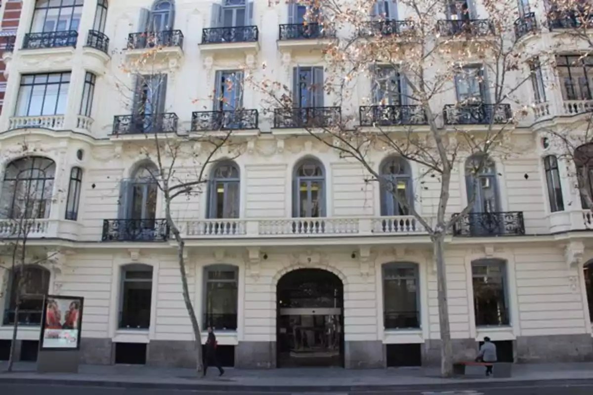 Fachada de un edificio antiguo de varios pisos con balcones de hierro forjado y árboles sin hojas en la acera Fachada de un edificio antiguo de varios pisos con balcones de hierro forjado y árboles sin hojas en la acera