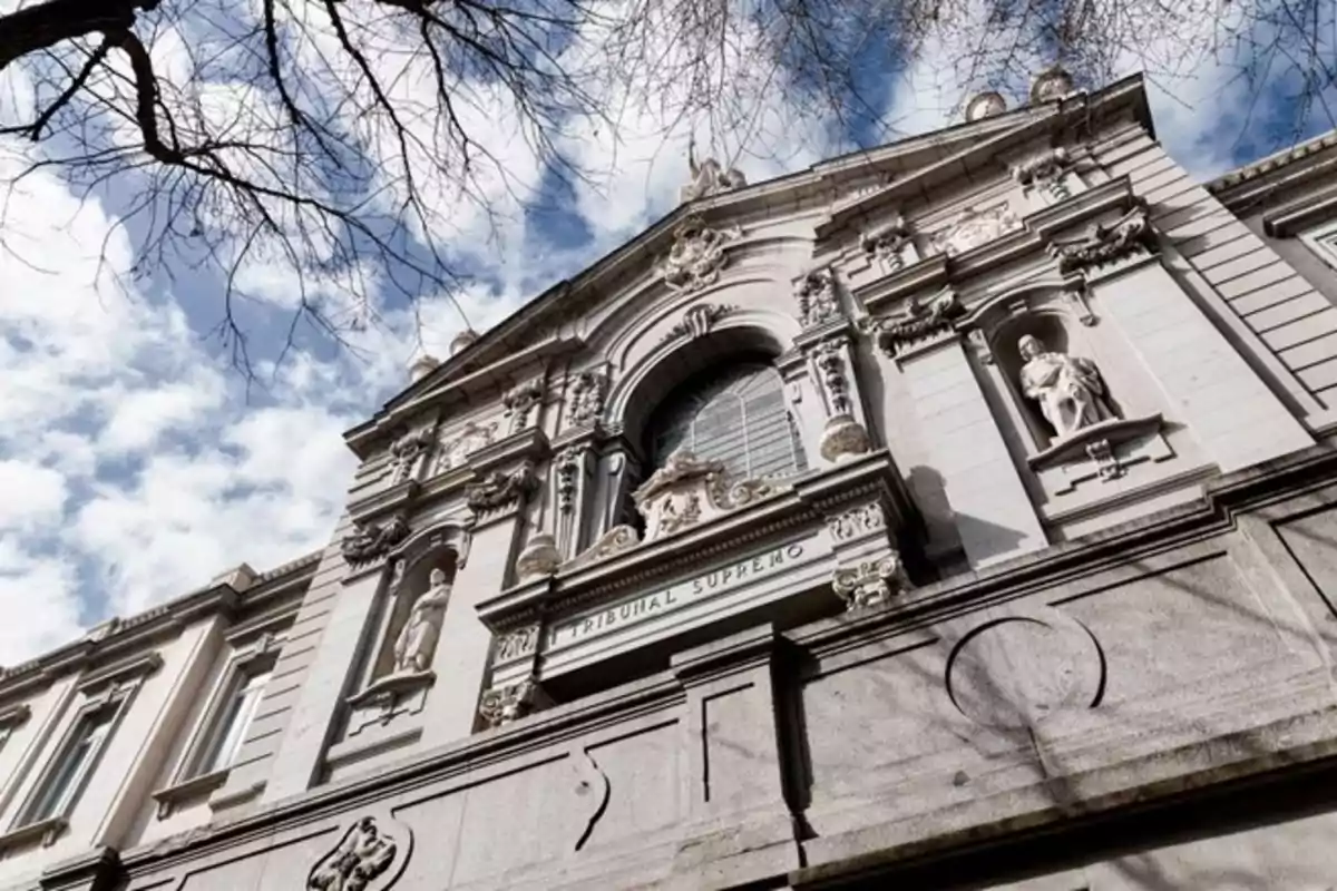Fachada del Tribunal Supremo de España vista desde un ángulo bajo con esculturas y cielo parcialmente nublado Fachada del Tribunal Supremo de España vista desde un ángulo bajo con esculturas y cielo parcialmente nublado