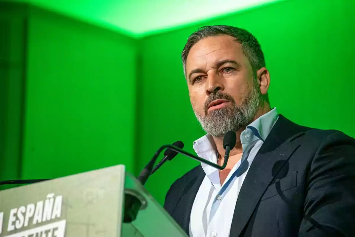 Hombre de barba y cabello corto hablando en un podio con fondo verde Hombre de barba y cabello corto hablando en un podio con fondo verde