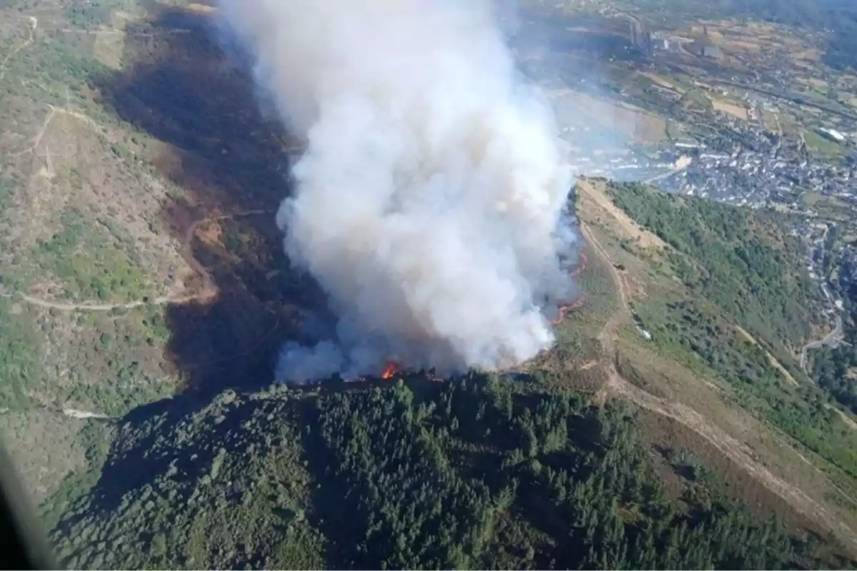 Incendio forestal en una zona montañosa con una gran columna de humo visible desde el aire y áreas verdes alrededor