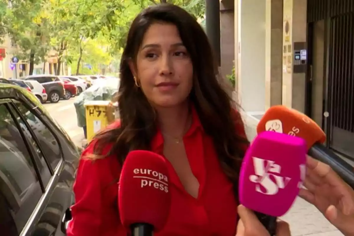 Mujer de cabello largo y oscuro con camisa roja siendo entrevistada por varios medios en la calle Mujer de cabello largo y oscuro con camisa roja siendo entrevistada por varios medios en la calle