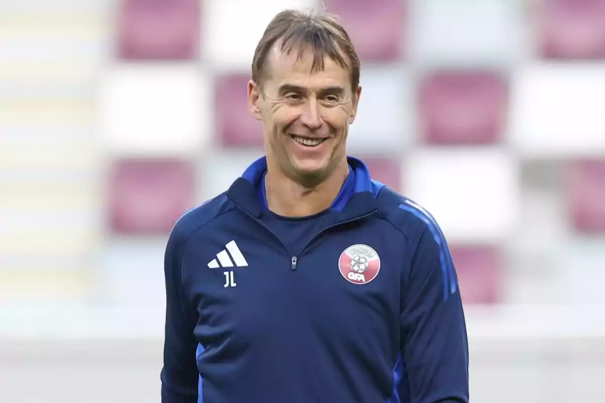 Hombre sonriente con chaqueta deportiva azul y fondo de gradas desenfocadas